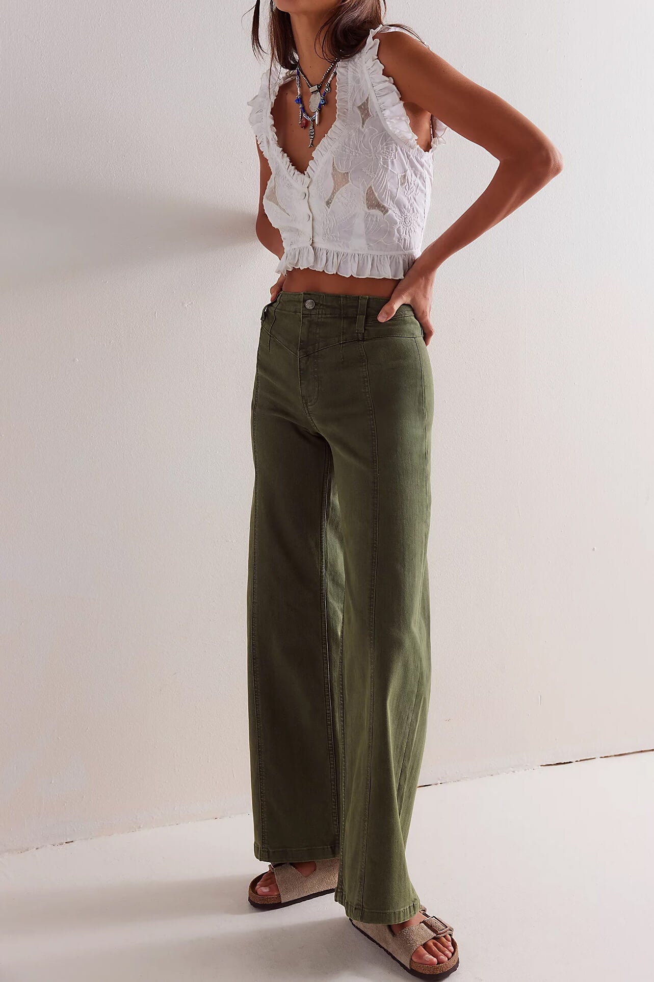 Person wearing a white lace top and green pants on a plain background