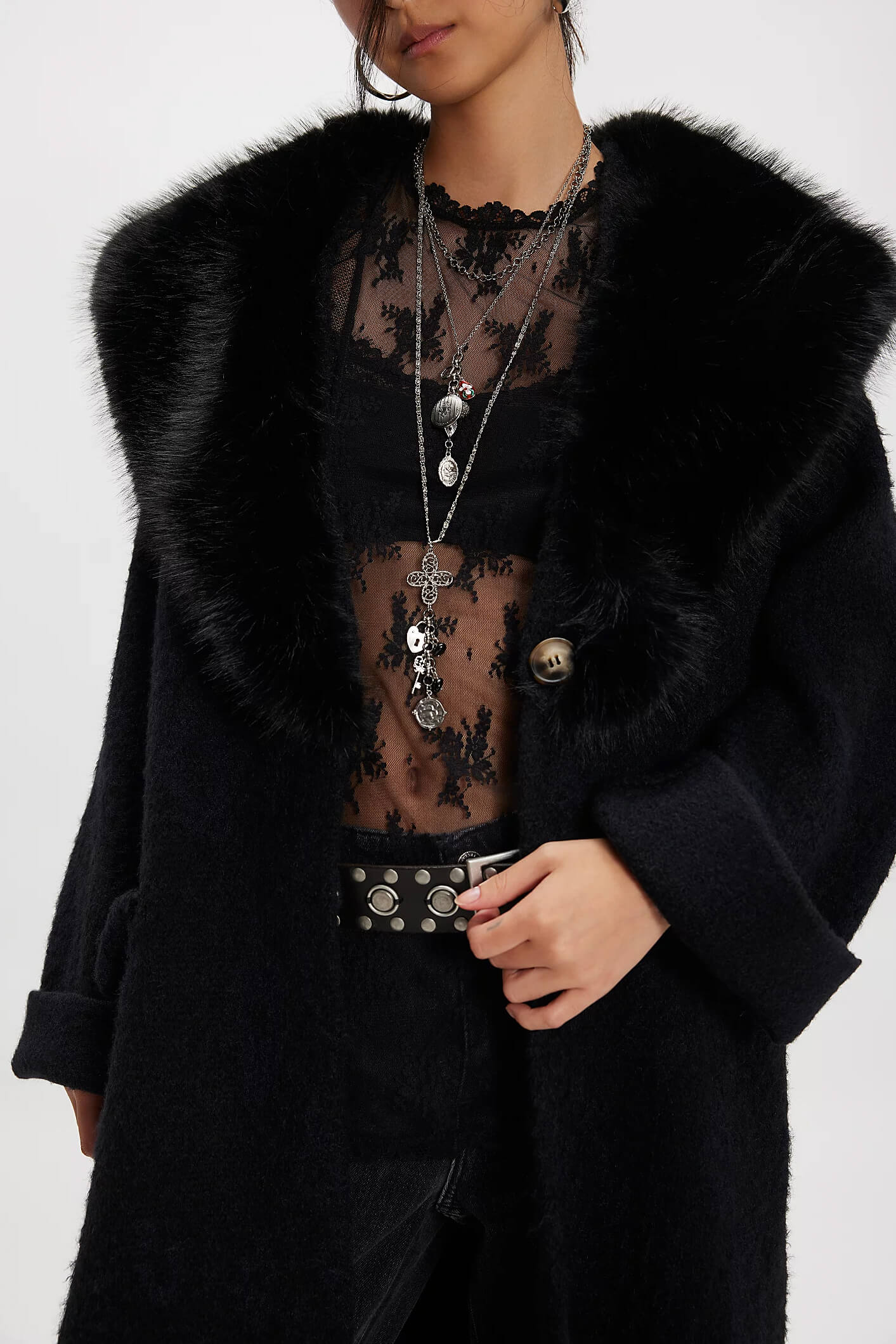 Person wearing a black coat with fur collar and sheer black top on a white background