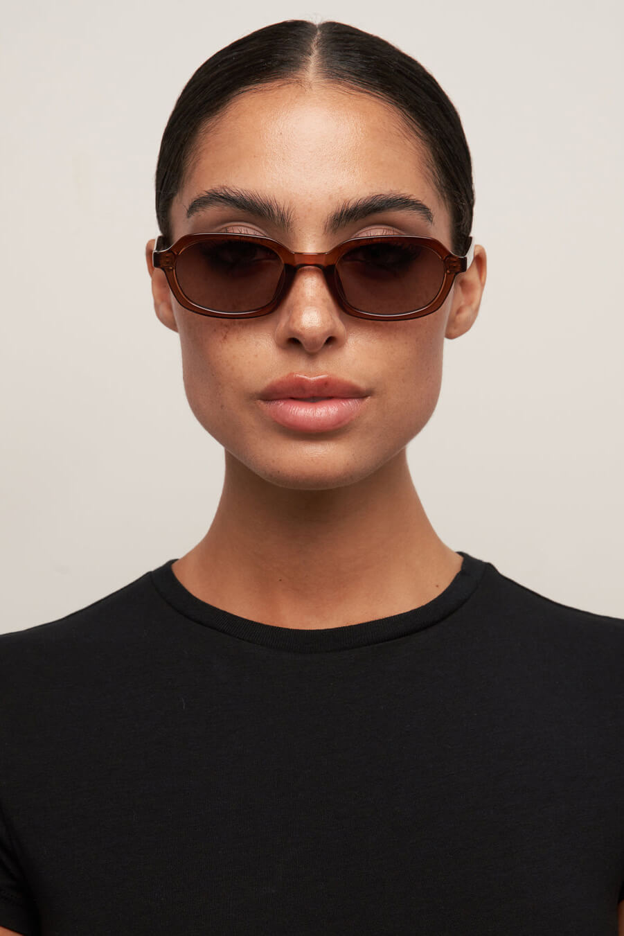 Person wearing brown sunglasses and a black shirt against a plain background