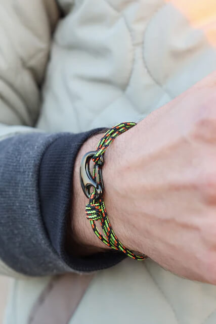 Bracelet with a clasp on a wrist, wearing a gray sleeve, against a neutral background.