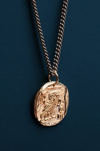 Gold necklace with a coin pendant on a dark blue background