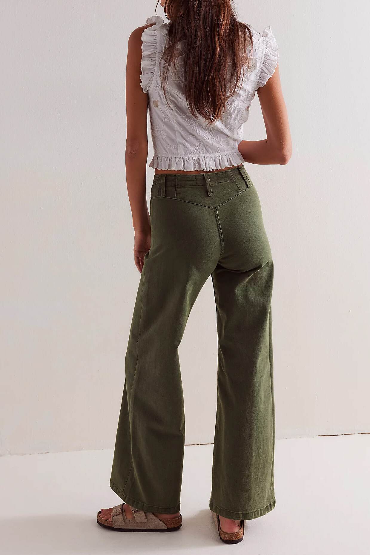 Person wearing a white ruffled top and green pants on a plain background