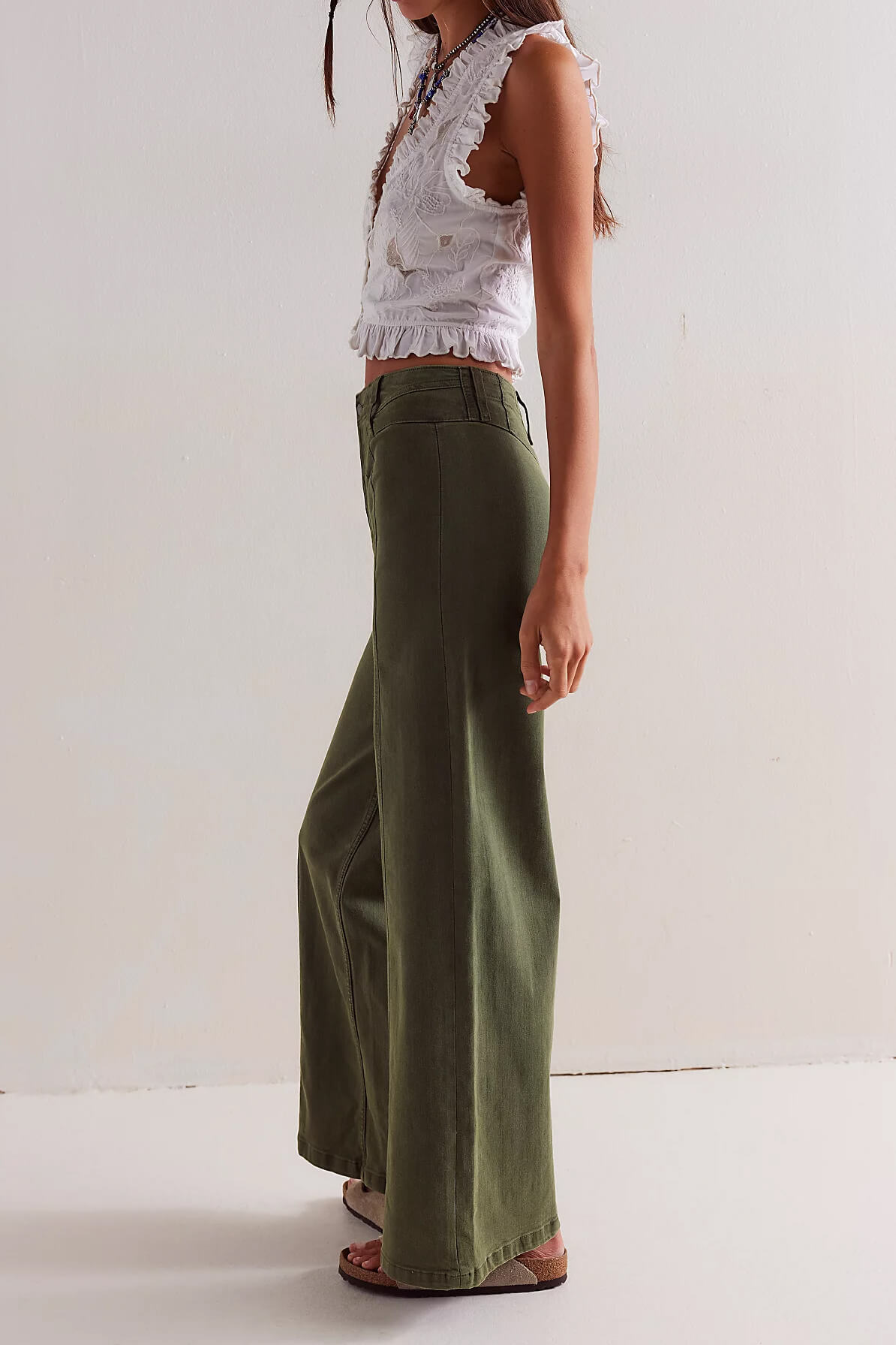 Person wearing a white lace top and green wide-leg pants on a plain background
