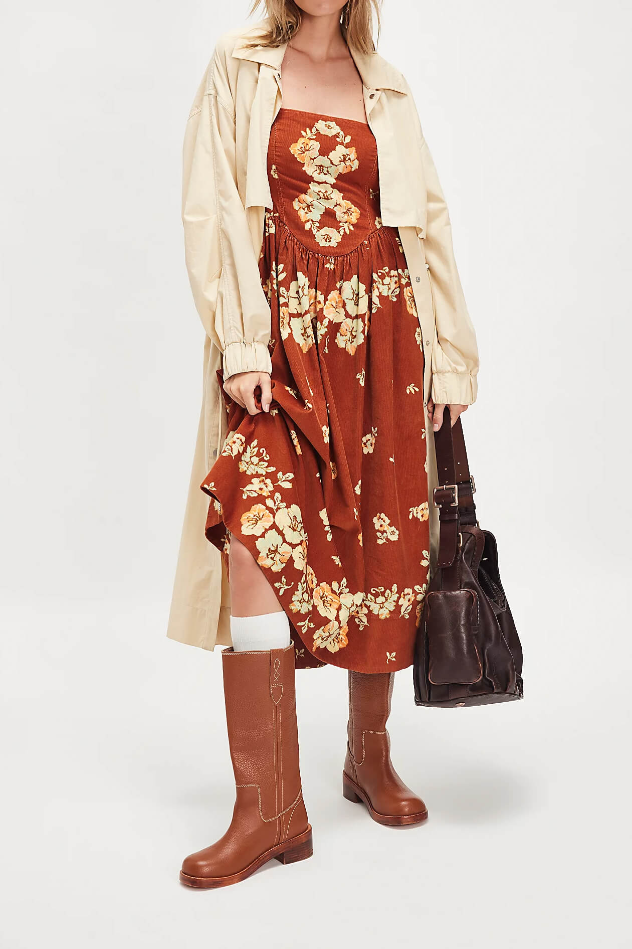 Woman wearing a floral dress, beige jacket, and brown boots on a white background