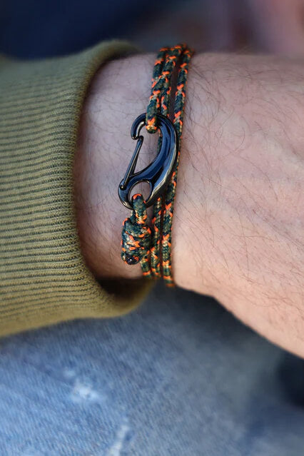 Bracelet with a carabiner clasp on a wrist, wearing a green sleeve and blue jeans.