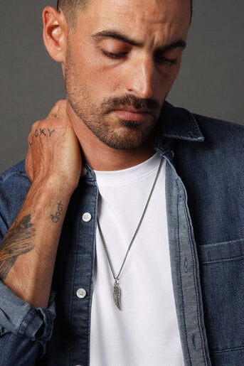 Man wearing a denim jacket over a white shirt with tattoos on his arm and neck.