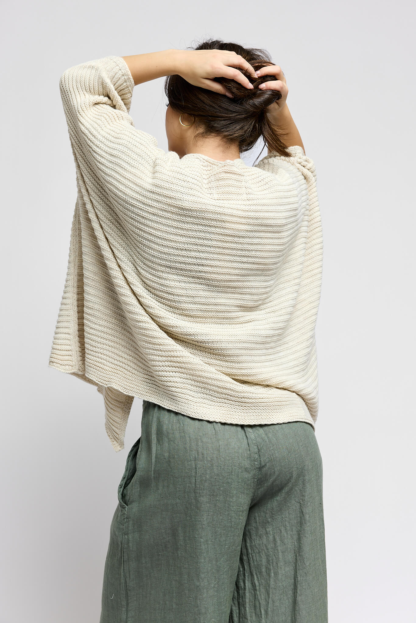 Person wearing a cream ribbed sweater and green pants against a white background